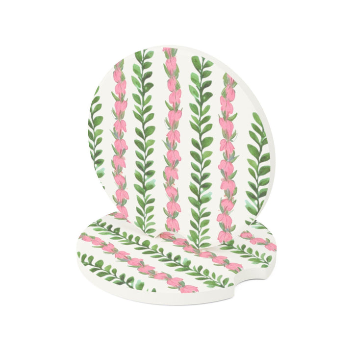two circular car coasters featuring a repeatingHawaiian flower lei pattern of pink flowers and green leaves.
