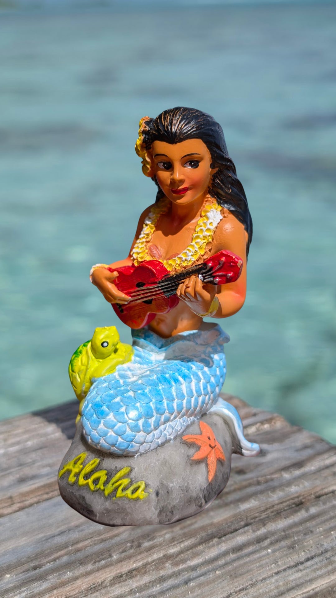 A figurine of a mermaid playing a guitar, with a turtle and starfish.