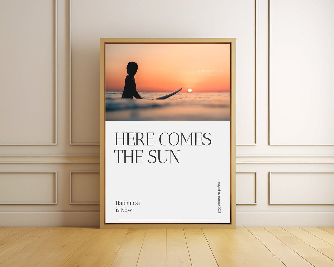 The image is a framed poster with a silhouette of a person surfing at sunset. The text on the poster reads "HERE COMES THE SUN" and "Happiness is Now".