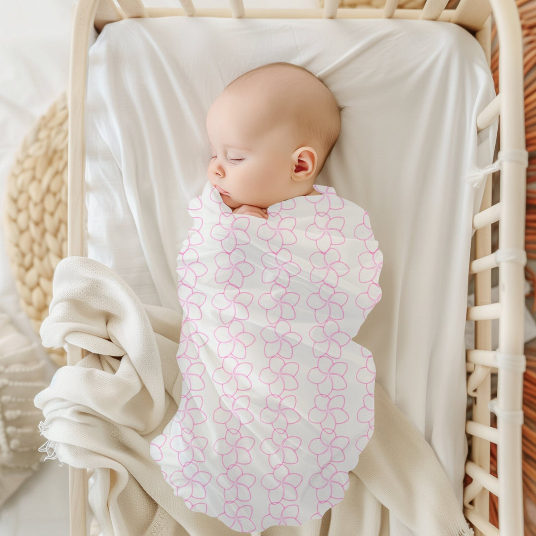 A sleeping baby swaddled in a pink Hawaiian flower lei floral blanket