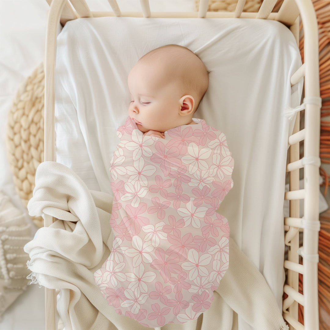 a baby peacefully sleeping in a white crib, wrapped in a pink and white floral blanket.