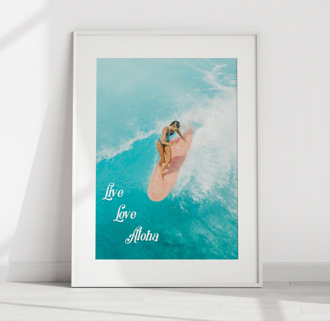 A framed photograph of a woman surfing on a wave, with the text "Live Love Aloha" written below the image.